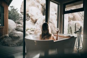roberto-nickson-unsplash- woman sitting in bathtub with glass in hand looking out the large windows - 1200 x 800