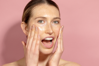 Adore Beauty - anti-aging skincare - woman with her mouth open and her hands on her cheeks. Background is pink - 1200 x 800
