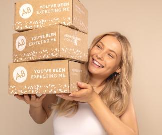 Best Festive Gifts Under 50 Dollars - blonde model is smiling and holding 3 boxes of Adore Beauty orders