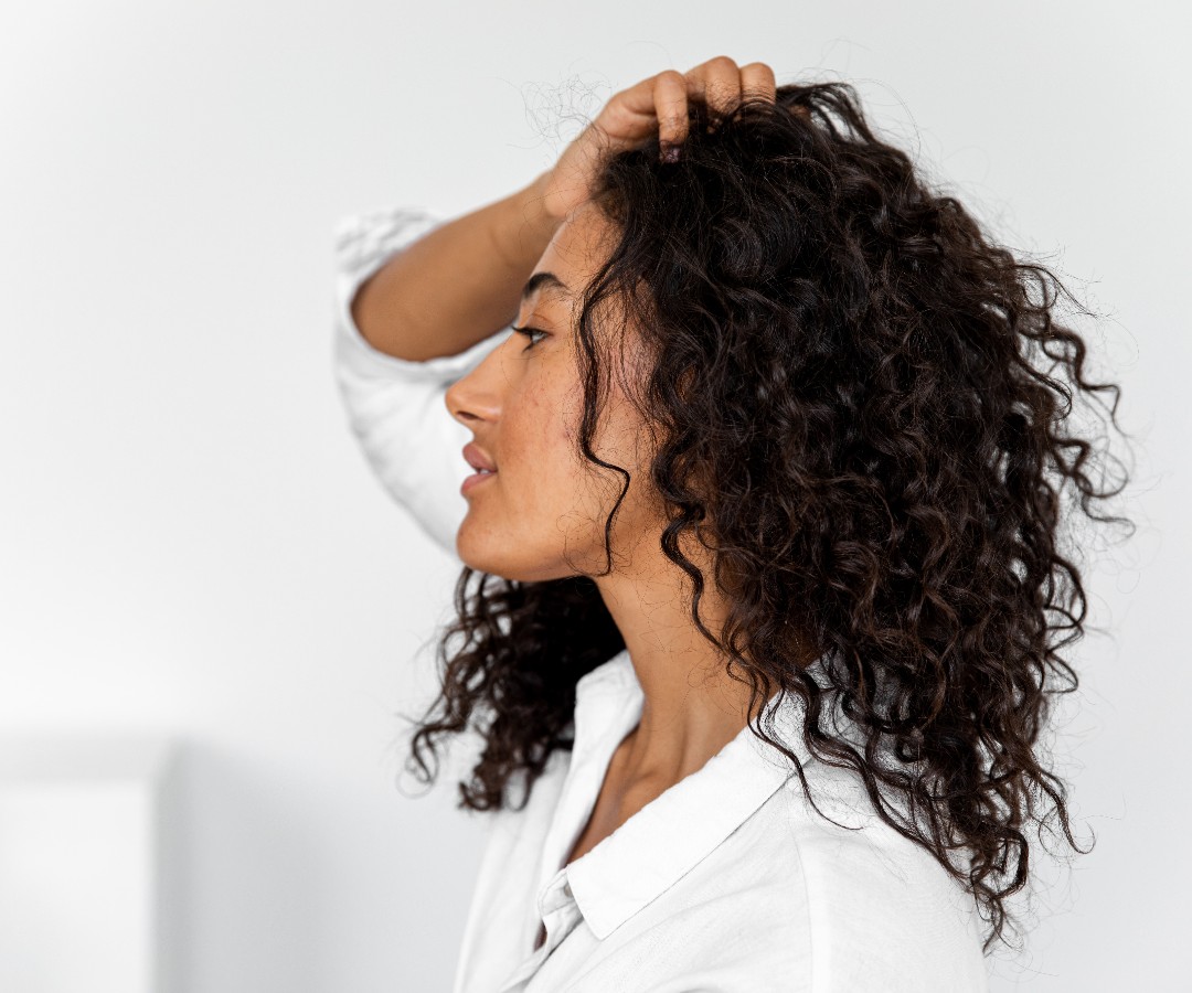 5 Tips for Taming Curly, Frizzy Hair Without Making it Greasy_side profile of a woman combing her fingers through long dark curly hair_1080x900