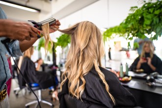 You’re Not Going To Believe The Results Of This Blonde Shampoo - woman with long blonde hair is sitting in hairdressers chair and a hairdresser is standing behind her and curling her hair with with hot tool - 2000 x 1333