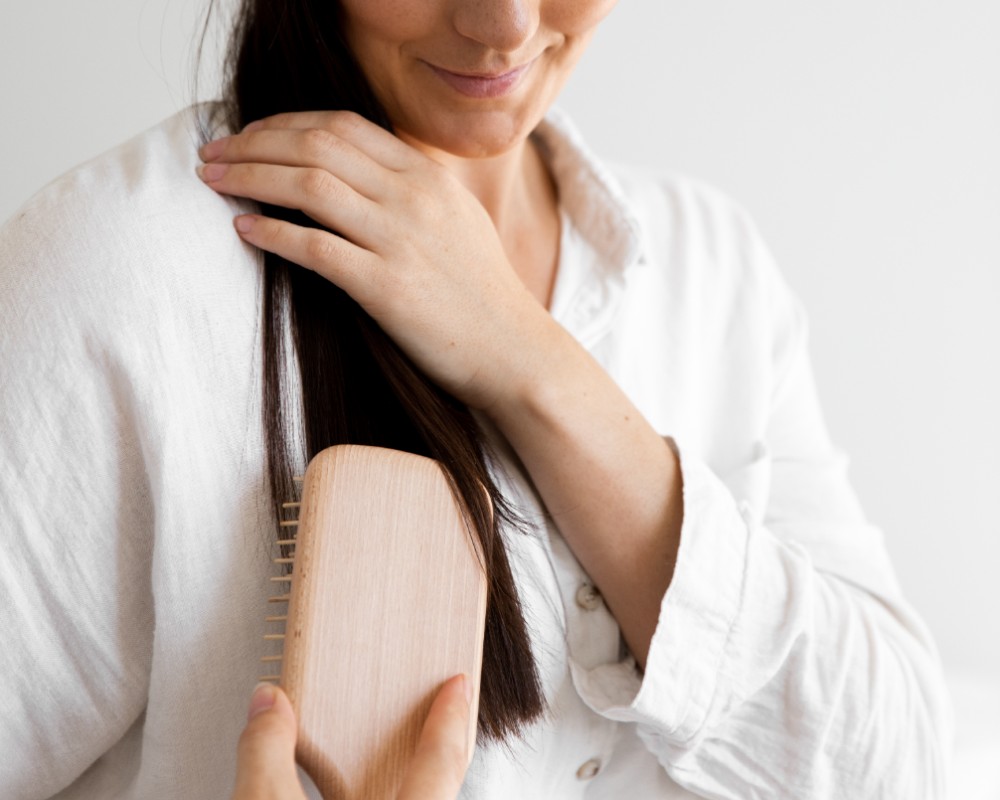 how to clean a hairbrush guide_woman in long sleeve white shirt is using a wooden paddle brush to comb through her long dark hair_1000x800