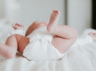 Baby in white onesie lays on their back on white sheet-1080x800
