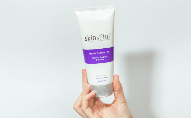 Skinstitut Glycolic Cleanser - hand holding product bottle up against white wall - 670 x 415