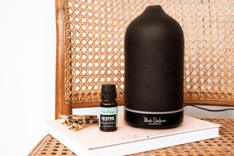 BlackChicken EssentialOil Diffuser - diffuser and small bottle of essential oil displayed on top of a book on a cane wicker chair - 1080 x 720