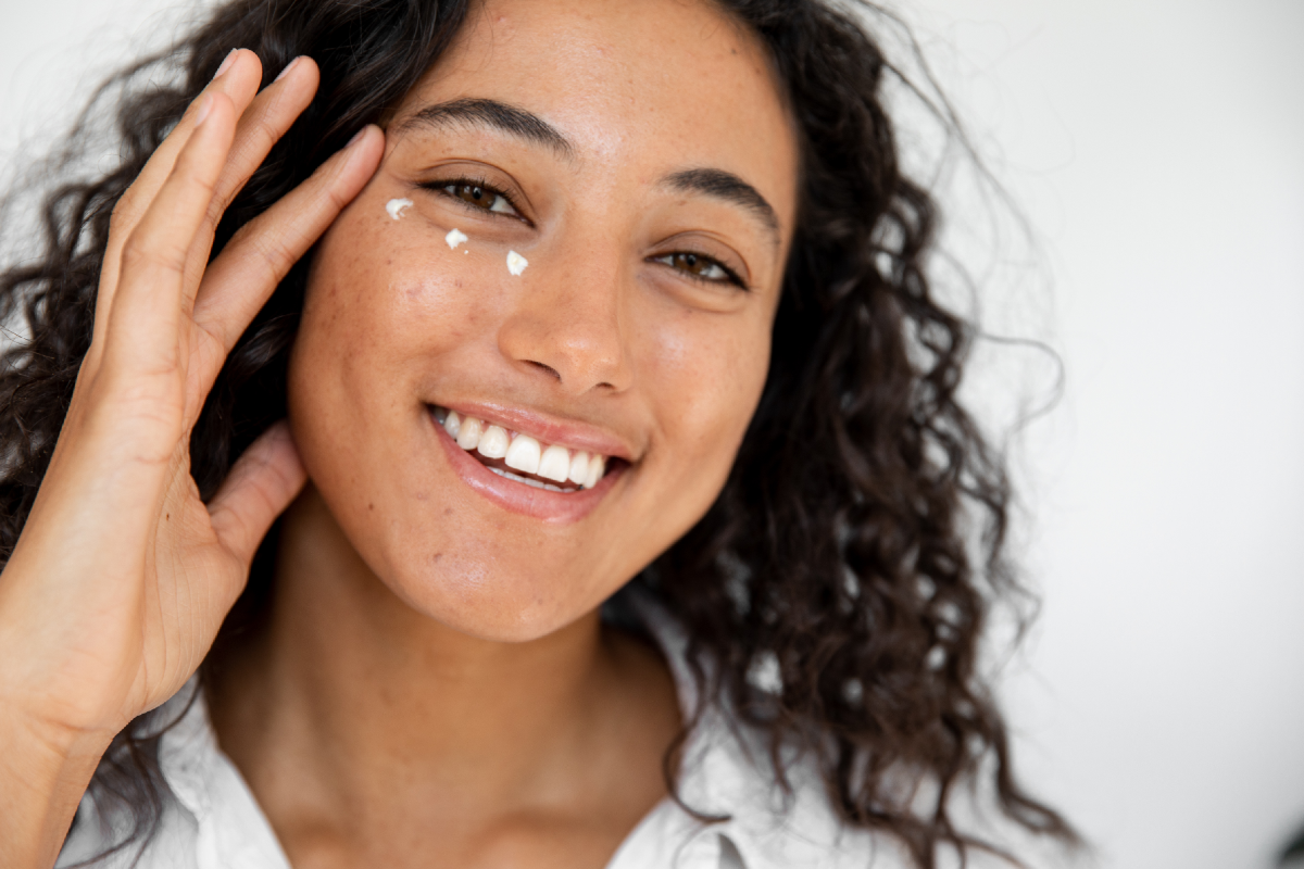 Adore Beauty - how to use eye cream for wrinkles - Woman with dark curly hair is smiling as she has 3 dots of eye cream under her eye - 1200 x 800