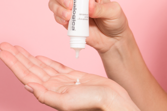 Adore Beauty - Dermalogica UltraCalming Serum Concentrate - one hand hold product bottle and squeezes out seru into palm of other hand. The background is light pink - 1200 x 800