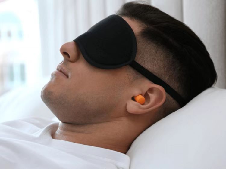 A man wearing earplugs and a sleeping mask