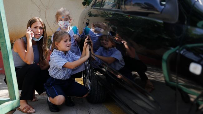 A Lebanese mother with her children hide behind a car from sniper fire outside a school, in the Christian neighborhood of Ain el-Remaneh.