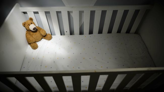 Teddy bear in an empty cot - PA Images