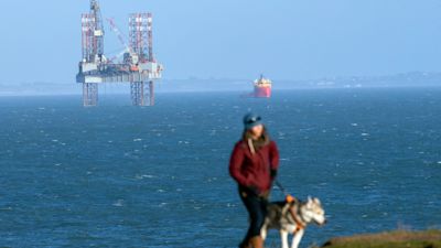 A clifftop dog walker passes the ENSCO-72 drilling rig in Poole Bay, off the coast of Dorset, where it is sinking an appraisal well on behalf of Corallian Energy to assess the potential reserves of oil in the 'Colter prospect', to the south of the existing Wytch Farm oilfield. Steve Parsons/PA