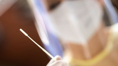 An employee at a test center holds a swab for a throat swab