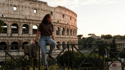 A woman sits on a fence outside the Colosseum in Rome, Italy.