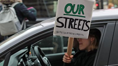 A woman holding a Reclaim the Streets placard out of the passenger window drives past New Scotland Yard in London, the day after clashes between police and crowds who gathered on Clapham Common on Saturday night to remember Sarah Everard. The Metropolitan Police has faced intense criticism for its handling of the vigil, with officers accused of "grabbing and manhandling" women during clashes with the crowd. Picture date: Sunday March 14, 2021.