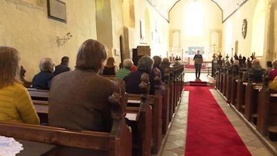 Campaigners sitting in church pews listening to someone talk from a lectern