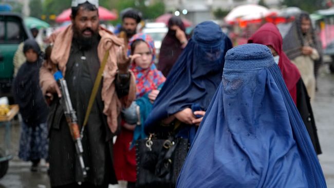 Afghan women walk through the old market as a Taliban fighter stands guard, in downtown Kabul,