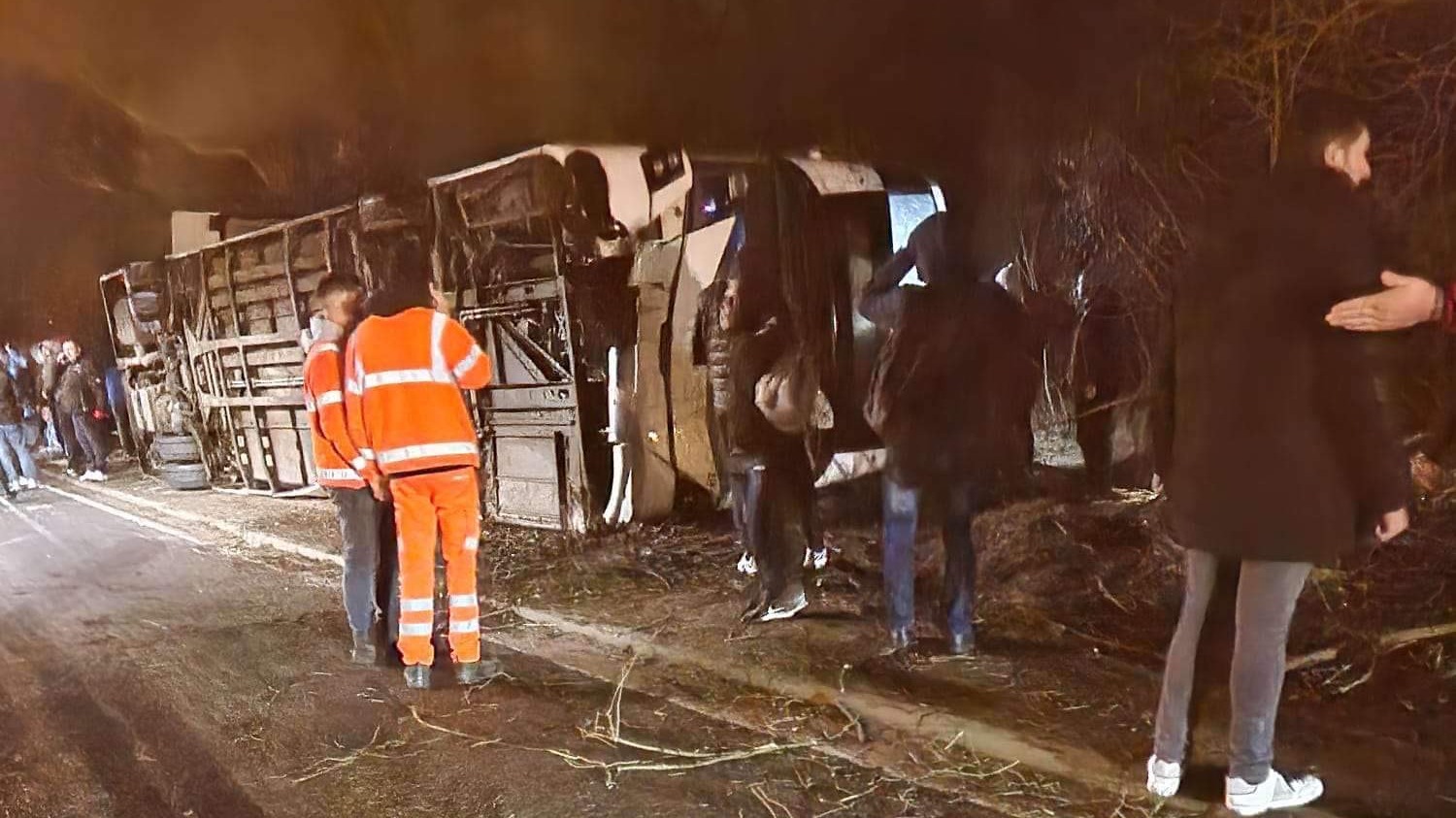 People stand outside around an overturned bus