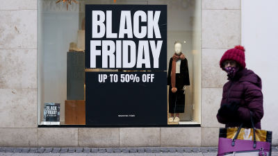 A woman standing outside a store with a sign advertising Black Friday deals.