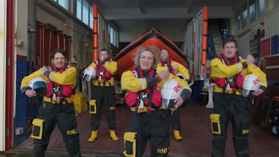 A group of RNLI crew standing outside the lifeboat house pounding their helmets
