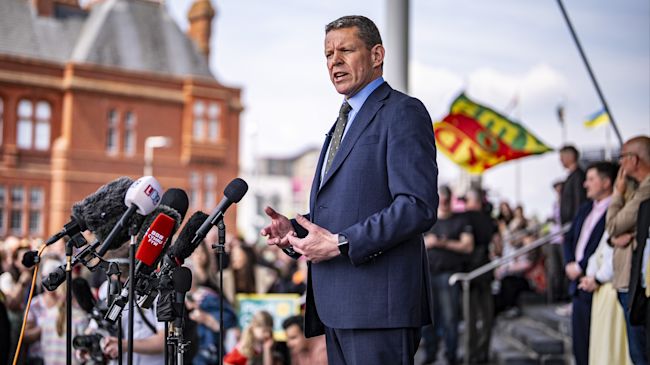 Rhun ap Iorwerth standing outside the Senedd after winning election. Crowds in the background
