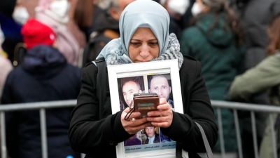 Syrian woman Yasmen Almashan holds the pictures of her five in Syria died brothers before the verdict in front of the court in Koblenz, Germany, Thursday, Jan. 13, 2022. The German court has convicted a former Syrian secret police officer of crimes against humanity for overseeing the abuse of detainees at a jail near Damascus a decade ago. (AP Photo/Martin Meissner)