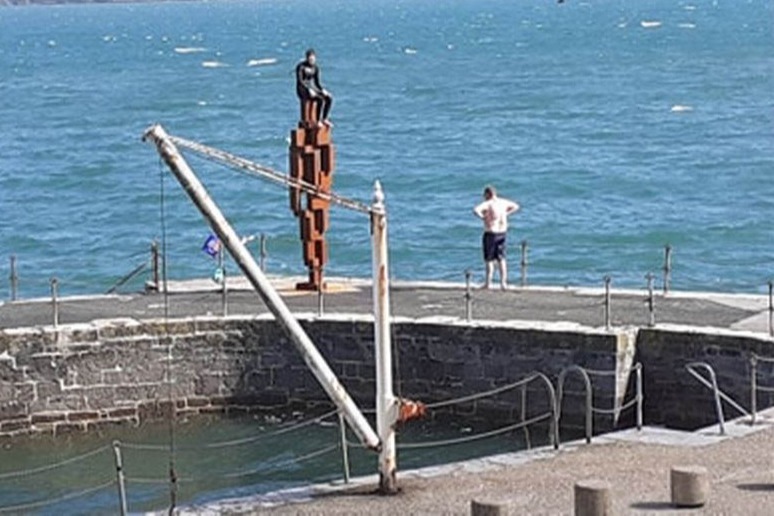 Two young people jumping off Plymouth's LOOK II statue into sea. 