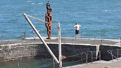 Two young people jumping off Plymouth's LOOK II statue into sea.