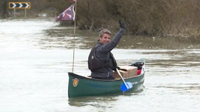 A man in a canoe on a flooded road looking behind him and waving