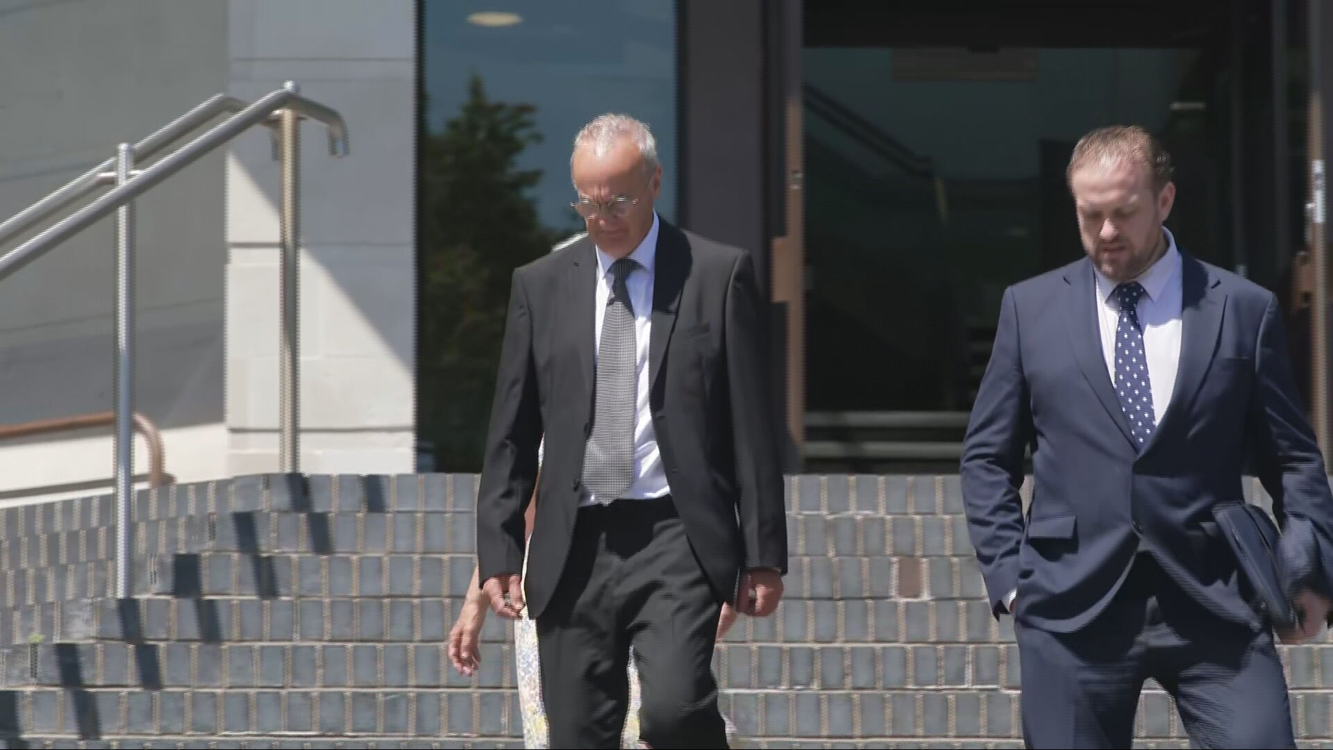 Robin Griffiths wearing a suit on the left walking down outdoor court steps