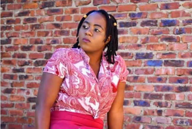 A photo of a woman sitting in front of a wall in a pink top and trouser