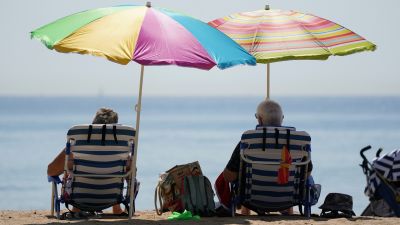 People sit under umbrallas as they enjoy the hot weather at Bournemouth Beach in Dorset.