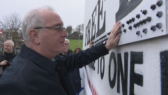 Richard Moore, who was blinded 50 years ago after being hit by a rubber bullet, reads the Braille slogan on Free Derry Wall.