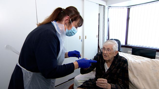 A carer helps 93-year-old Wilf Johnstone with his hearing aid