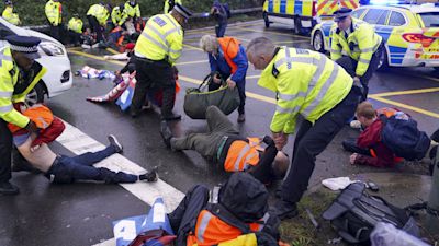 Police officers detain a protester from Insulate Britain occupying a roundabout