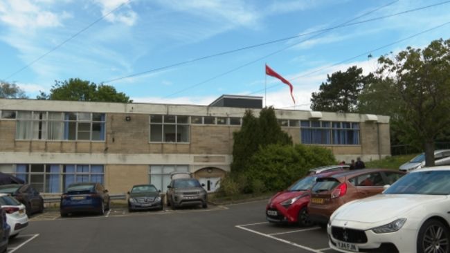Two storey former school building with a Hindu flag flying from it and cars parked in front of it.