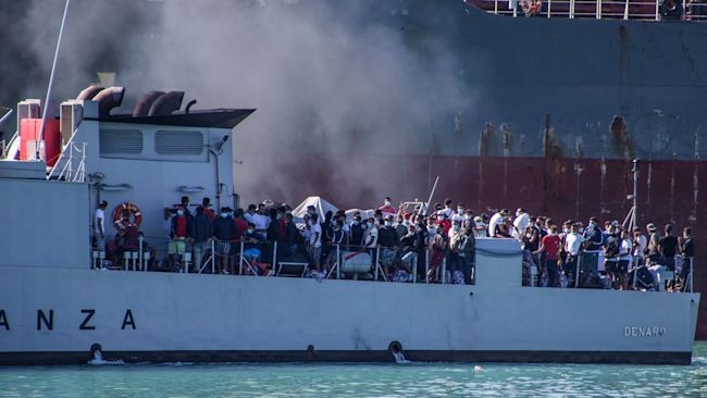 migrants arrive in Porto Empedocle, Sicily, aboard two military ships after being transferred from the island of Lampedusa. Sicily's governor has ordered all migrants to be transferred from the island by Monday, part of push-back by Italian regions alarmed by last week's surge in COVID-19 cases. On Saturday, Italy registered 1,071 new cases, the highest daily number since mid-May, and only weeks after the nation had seen the number of day-to-day new infections plunge to about 200. (Fabio Peonia/LaPresse via AP)