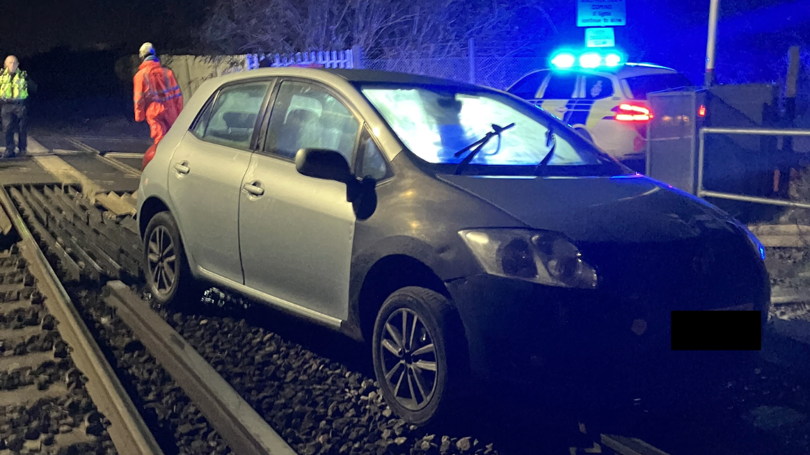 Car crashes through level crossing barriers and ends up on train tracks
