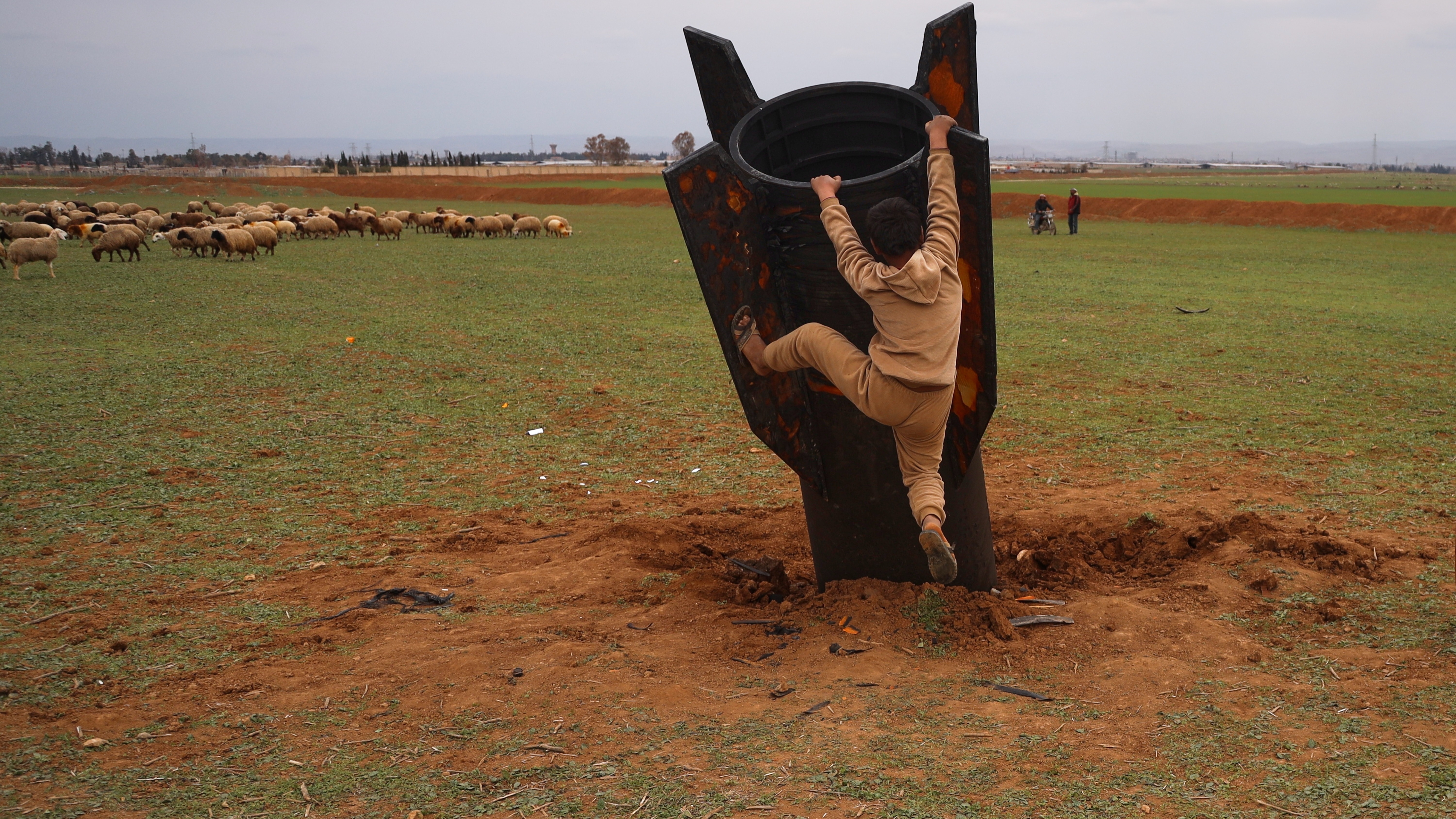 a boy tries to climb on an unexploded Iranian projectile that landed in an open field in the outskirts of Qamishli, eastern Syria