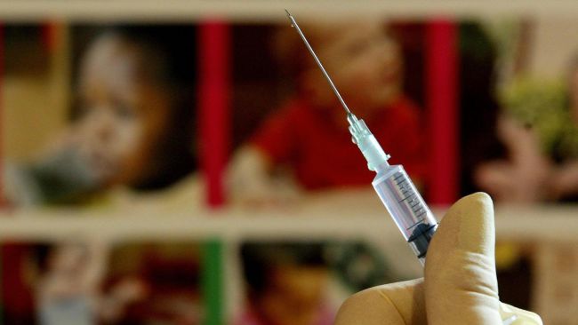A medical professional holds a syringe containing an MMR jab.