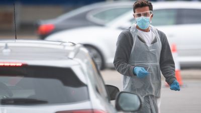 A worker prepares to swab a person in a car at a drive-through testing facility.