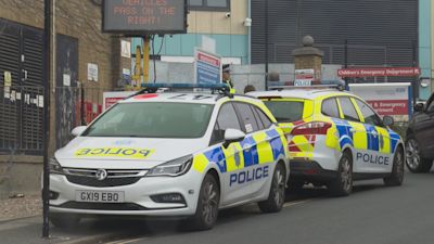 Two police cars parked back to back along a hospital side road.