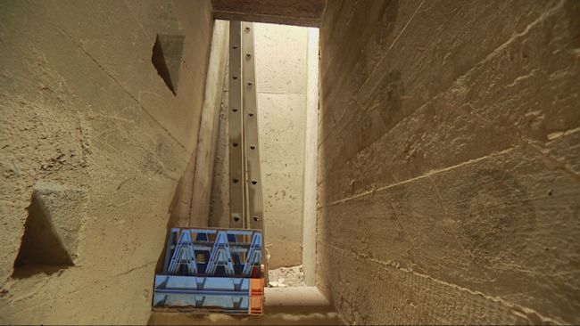 A hatched entrance to an underground corridor with light coming down, with a ladder allowing people to climb down and in.