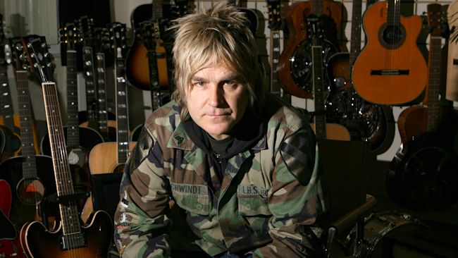 Mike Peters, the Alarm frontman sat infront of lots of guitars.