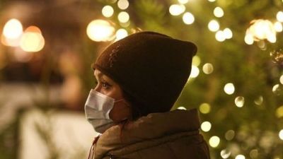 A woman in a protective mask near Christmas lights.