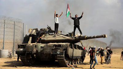 Palestinians wave their national flag and celebrate atop a destroyed tank at the Gaza Strip fence.