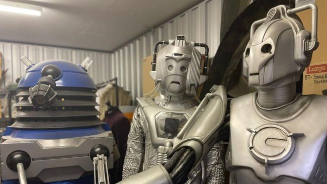 A blue dalek and two cybermen stand next to each other