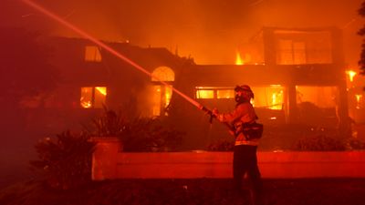 A firefighter works to put out a structure burning during a wildfire in Laguna Niguel