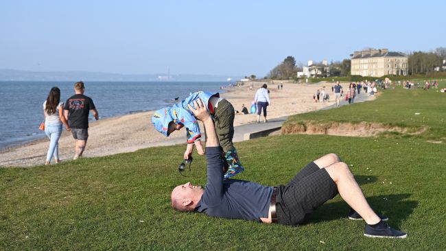 People enjoy the good weather at Seapark, Holywood, Northern Ireland, with Belfast in the distance. Picture date: Saturday March 26, 2022. See PA story WEATHER Spring Ireland. Photo credit should read: Michael Cooper/PA Wire