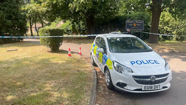 A police car in a shaded wooded area.