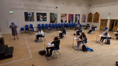 Students sat at individual desks in a school hall 